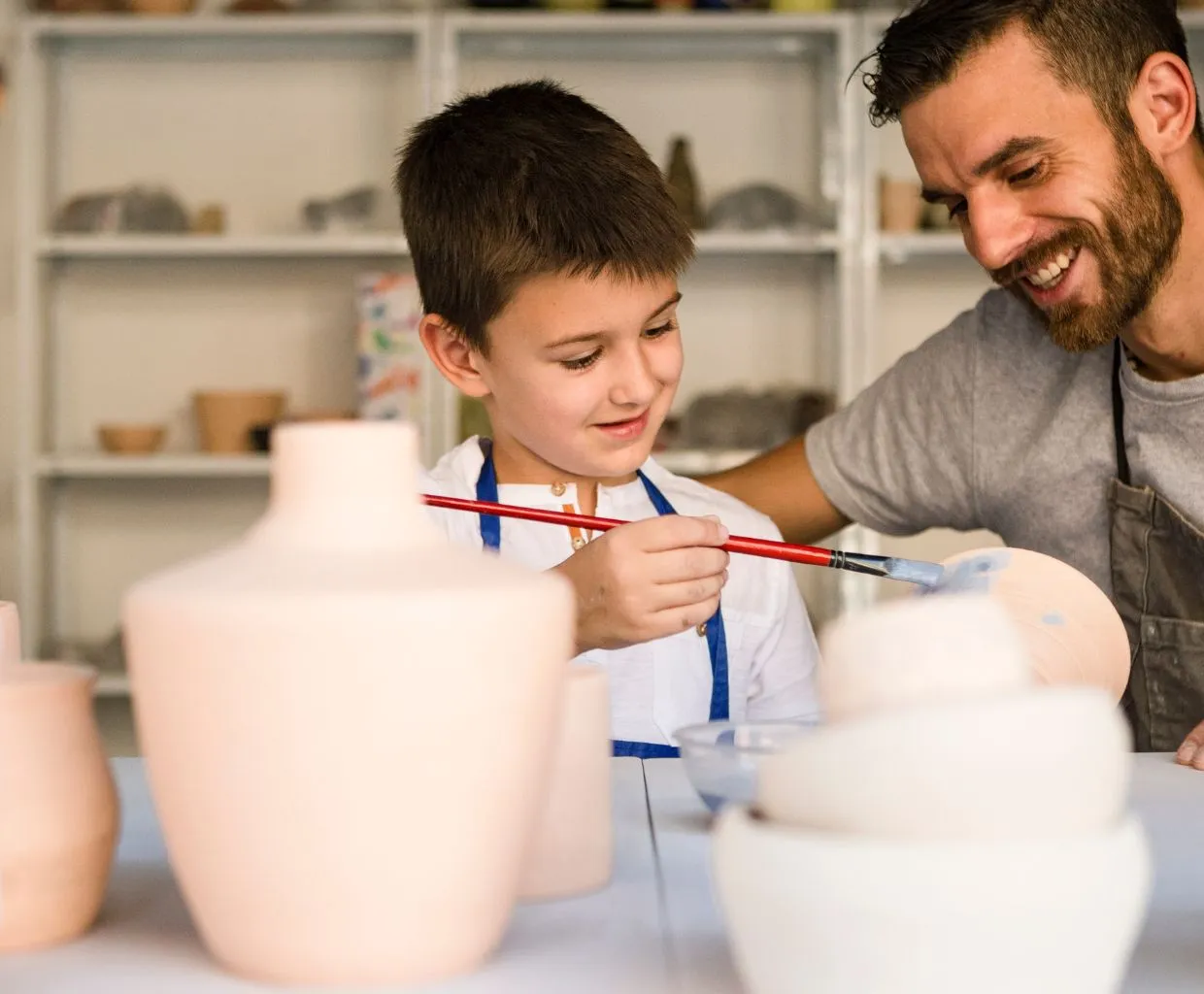 Niño pintando una pieza de cerámica junto a un adulto en un taller