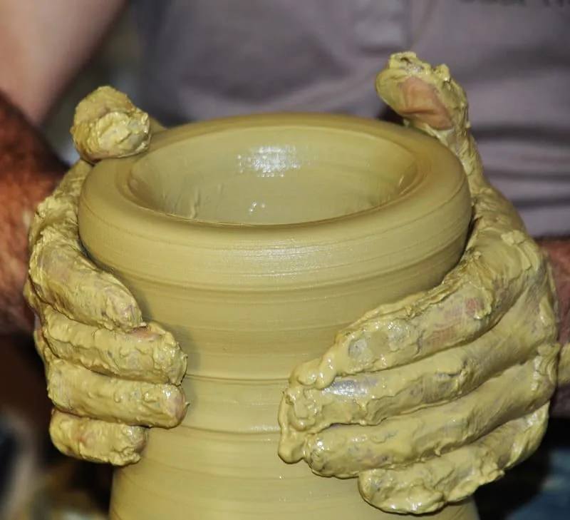 Manos sosteniendo una pieza de arcilla cubierta de engobe amarillo