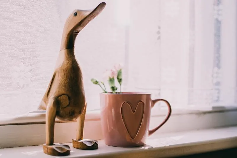 Figura decorativa de un pato de madera junto a una taza