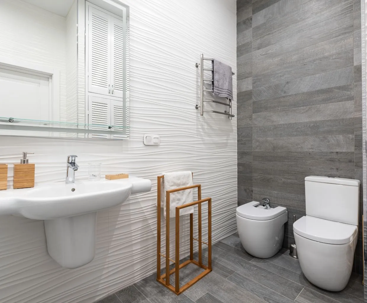 Baño con paredes de azulejo blanco, lavabo, inodoro y toallero de madera