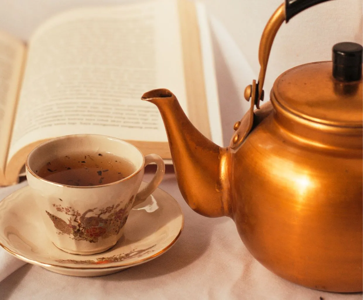 Taza de porcelana decorada con su plato junto a una tetera de cobre